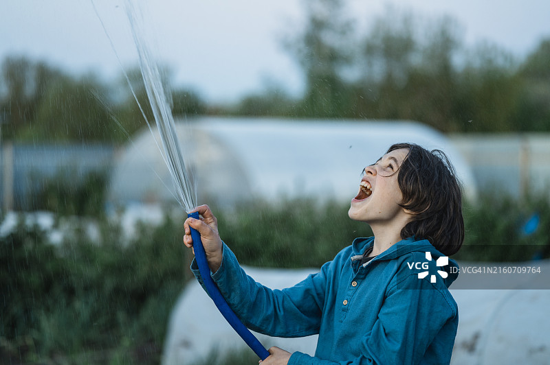 男孩在温室旁喷水玩耍。图片素材