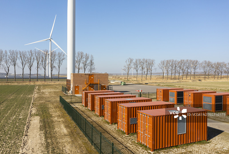 田野上树木和风力涡轮机旁边的巨大红色电池容器图片素材