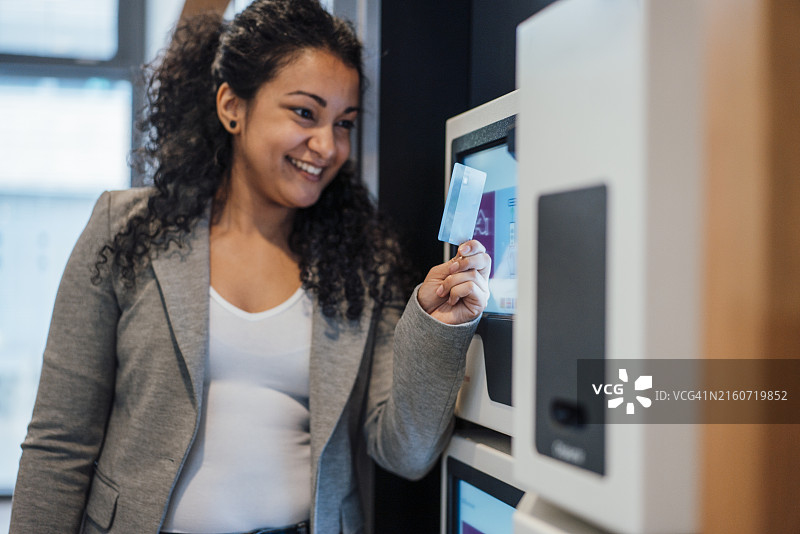 微笑的女商人拿着信用卡站在ATM机旁图片素材