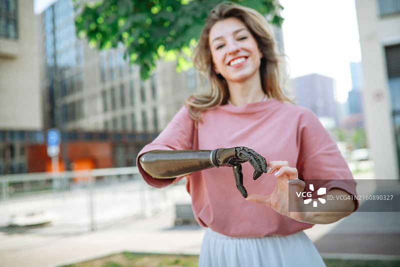 年轻女人用假肢手臂在城市公园里用手做出心形，表达感激和个人力量图片素材