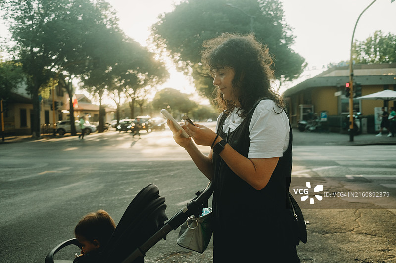 母亲在日落时分推着婴儿车使用智能手机图片素材