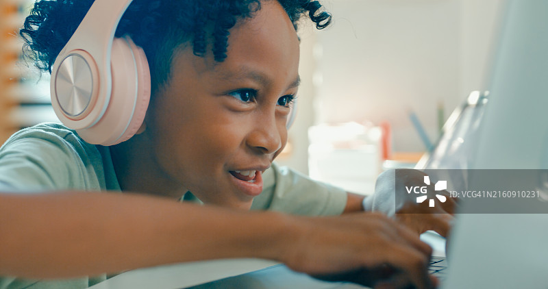 充满热情的年轻非裔美国男孩使用笔记本电脑和数位板与在线课程互动，完全沉浸在家庭教育活动中图片素材
