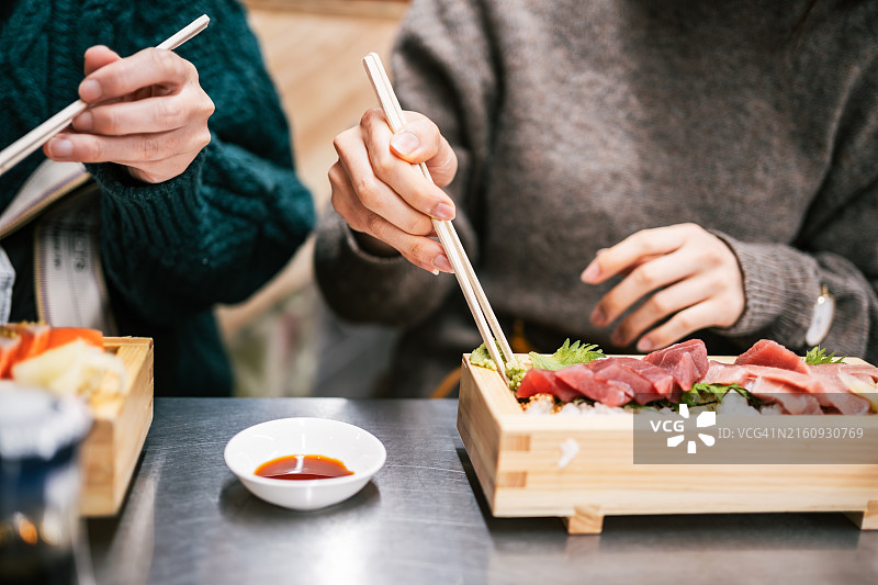 女人用筷子在传统日式餐盘上享用新鲜生鱼片图片素材