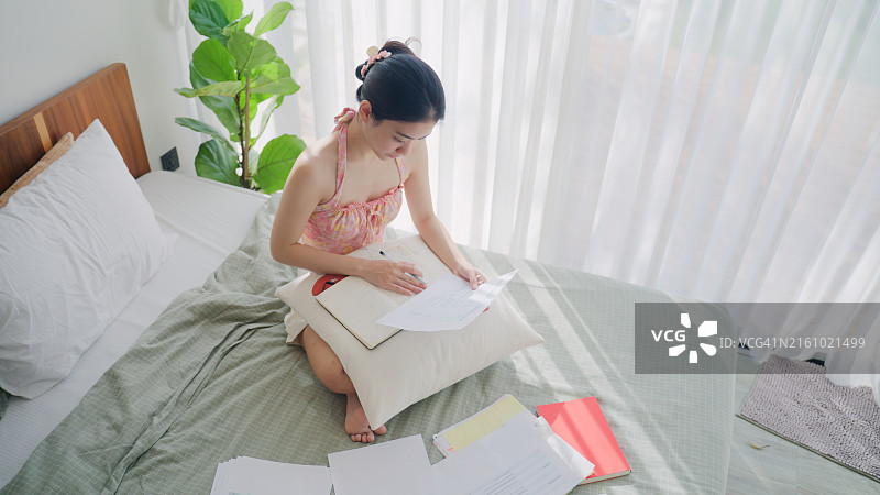 Z世代女性金融顾问在舒适的卧室里审查财务文件，阳光明媚，亚洲女性在家办公，处理公司业务的财务和会计图片素材