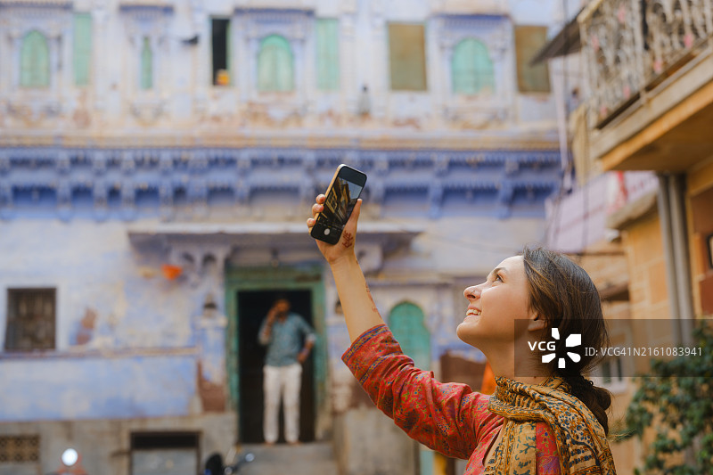 在印度焦特布尔蓝色之城旅行时用智能手机拍照的女人图片素材