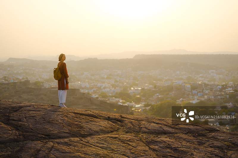 女人站在城墙上眺望日落时分的焦特布尔城市景观图片素材