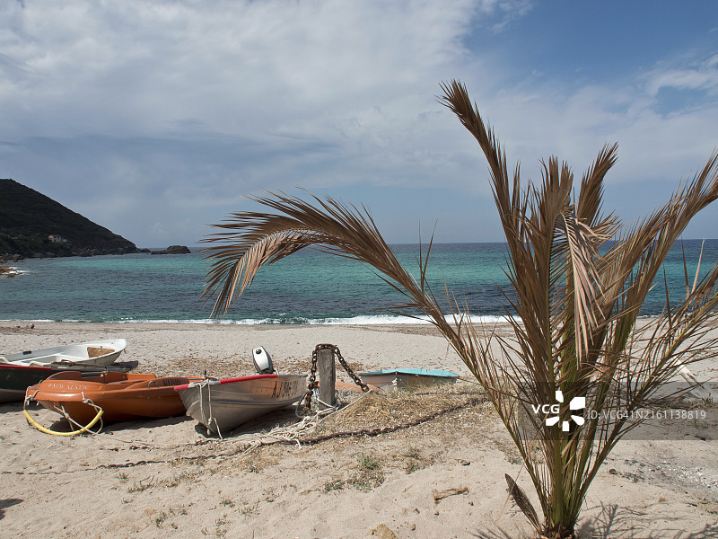 法国科西嘉岛阿雅克肖：前景是沙滩、船只和棕榈树，背景是海洋和有云的蓝天图片素材