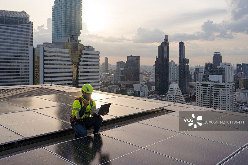 电气技术员使用平板电脑监控城市屋顶建筑上的太阳能电力系统运行，他正在通过对讲机进行通信。图片素材