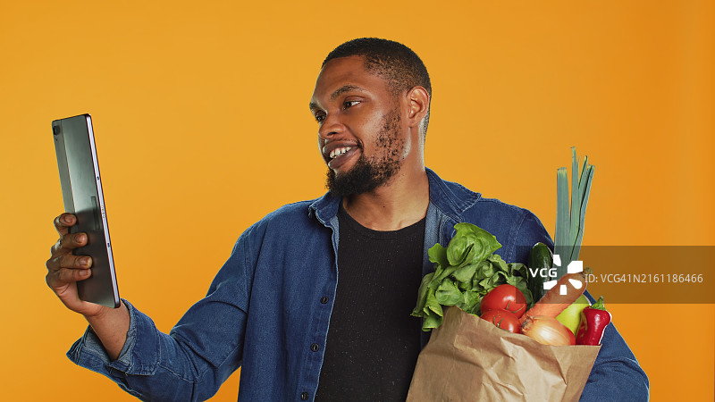 拿着食品杂货，以橙色为背景的年轻男人图片素材