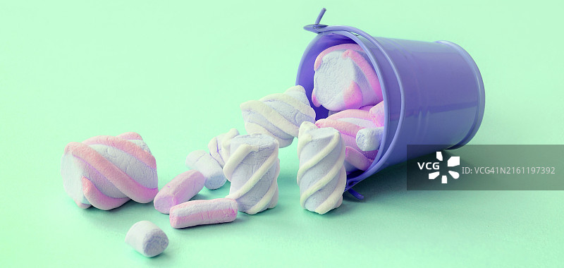 倾倒的装满棉花糖的丁香色迷你桶，位于青绿色粉彩背景上图片素材