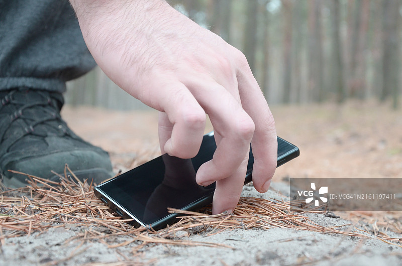 男人在秋季冷杉木小路上捡起丢失的手机，寻找失物概念图片素材