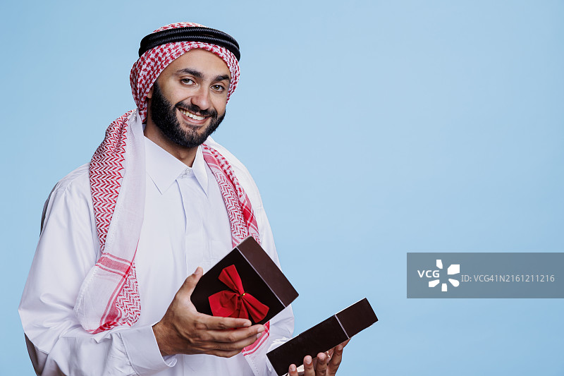 穿着传统服装，拿着礼品盒的男人，背景为蓝色图片素材