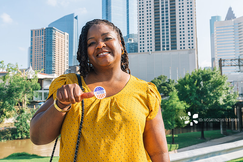 快乐的黑人妇女拿着一张“我投票了”的贴纸，参加总统、参议员、国会或地方选举图片素材