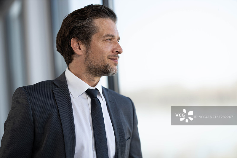 面带微笑的男商人靠窗做白日梦图片素材