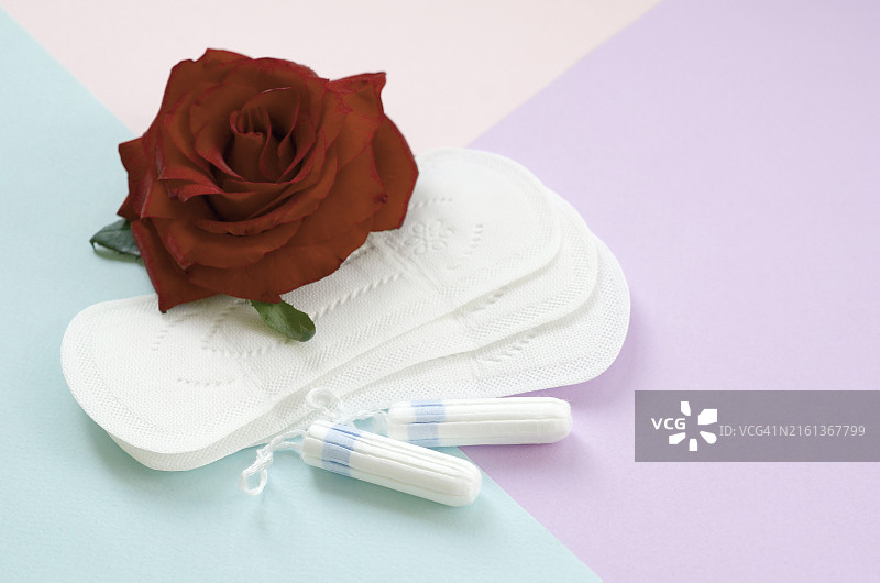 月经垫和卫生棉条与红色玫瑰花在彩色背景上图片素材