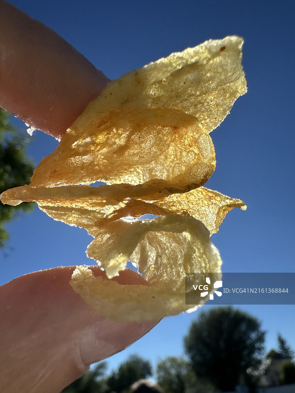 手指夹着炸薯条的细节，对着蓝天，非常开胃和酥脆图片素材