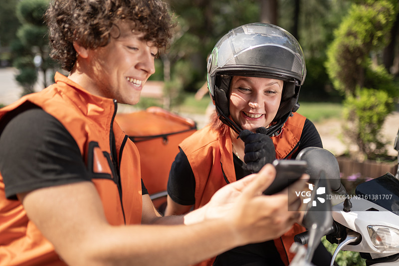 快递员坐在摩托车上聊天并展示手机内容图片素材