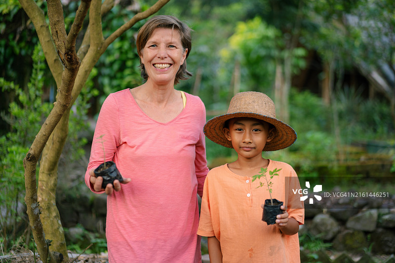 白人女性和东南亚男孩一起拿着树苗准备种植图片素材