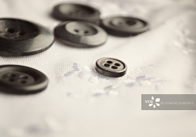 白色绣花织物上散落的琳·兰德尔黑色纽扣图片素材