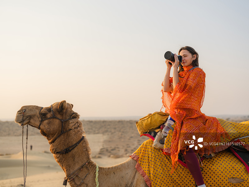 女人在沙漠骑骆驼时用相机拍摄日落图片素材