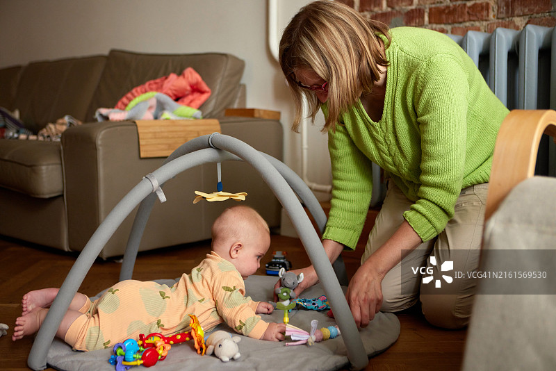 温馨的客厅里，女子在游戏垫上与婴儿互动图片素材