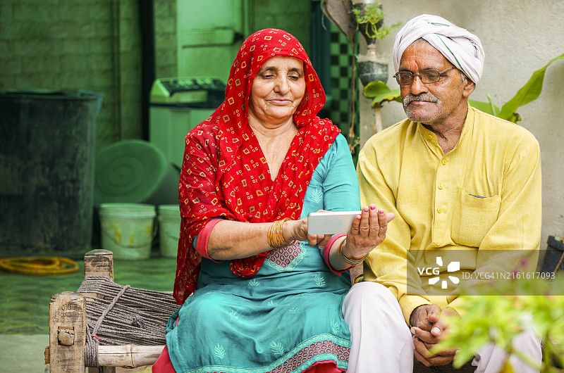 快乐的印度老年夫妇坐在床上一起使用智能手机图片素材