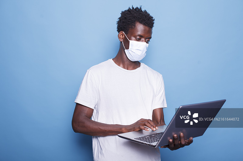 年轻男人在蓝色背景下使用笔记本电脑图片素材