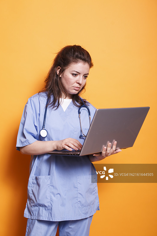 橙色背景下使用笔记本电脑的女医生图片素材