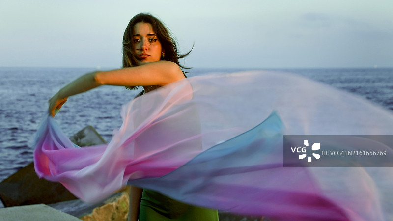 年轻女子手持彩色面纱在风中摇曳图片素材