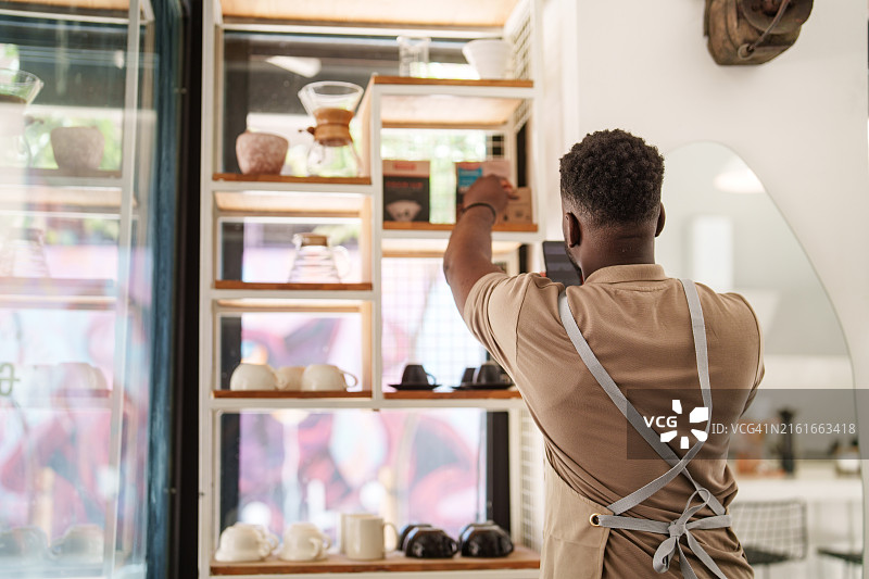 咖啡店员工整理零售展示架上的烘焙咖啡包装图片素材