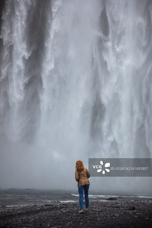 红发女子走向冰岛维克的斯科加瀑布图片素材