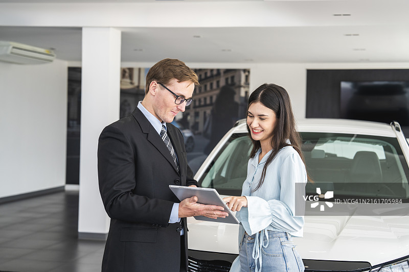 汽车销售员在展厅向女人展示平板电脑功能图片素材