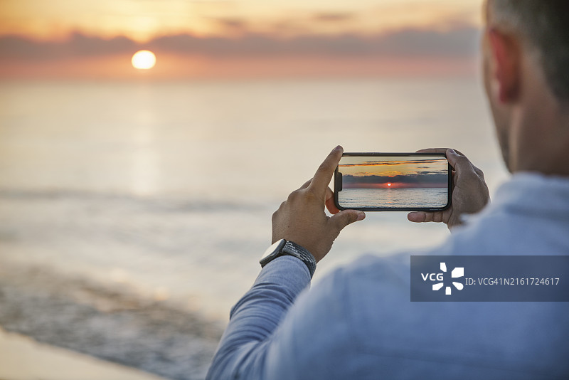 男子在海滩上用智能手机拍摄黎明的背影，波兰赫尔图片素材