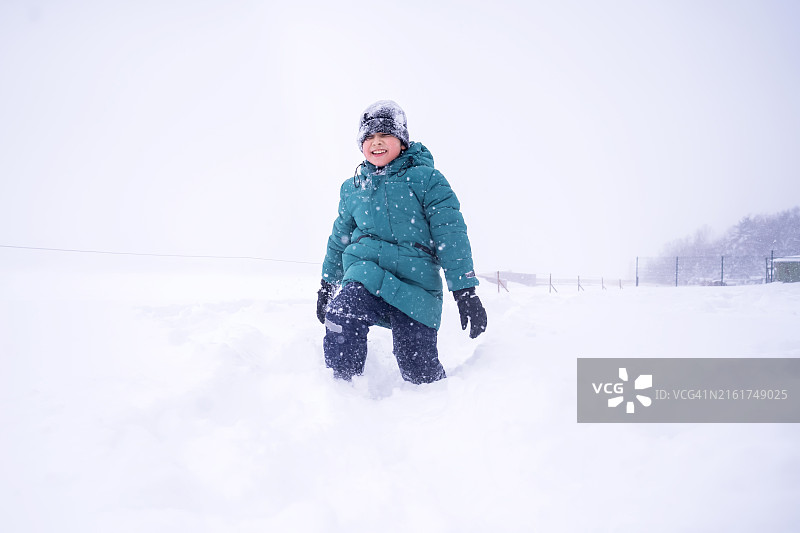 穿着暖和冬装的男孩走过白色的蓬松雪堆，冬季散步图片素材