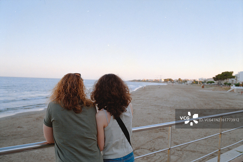母女在海滩栏杆旁眺望大海，胶片摄影图片素材