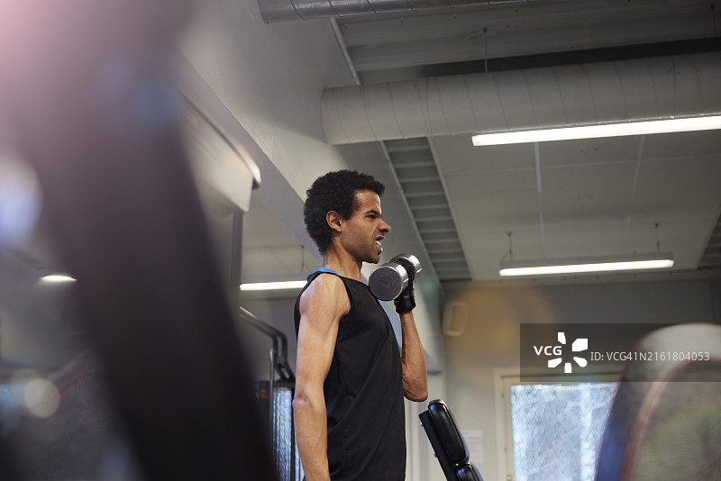 青年男子在健身房里做鬼脸，同时用哑铃锻炼图片素材