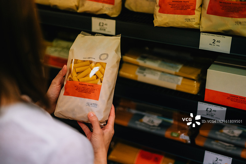 年轻女人在超市里看货架上意大利面的营养标签图片素材