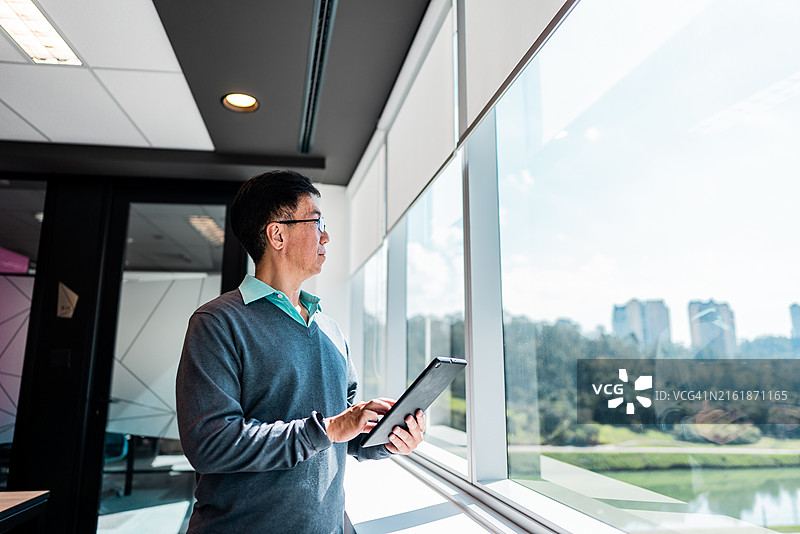 在办公室靠窗使用平板电脑的商人图片素材