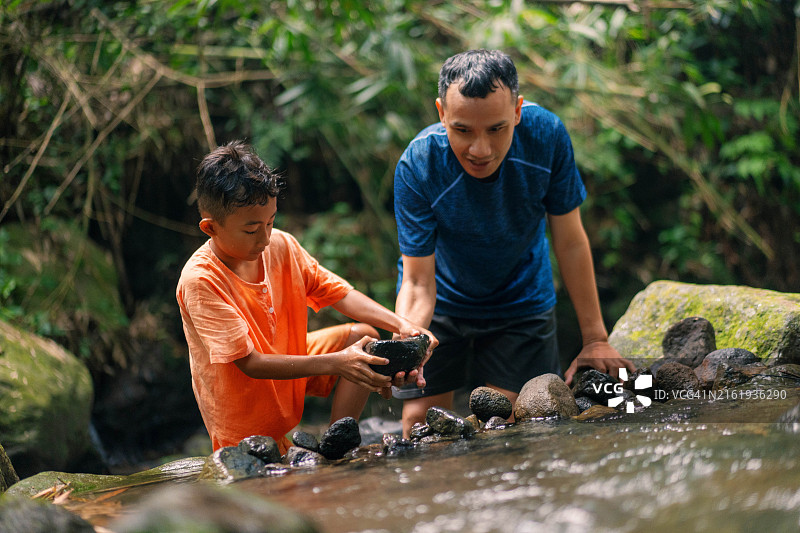 青春期前的男孩在浅河中和父亲一起玩耍，建造岩石水坝图片素材