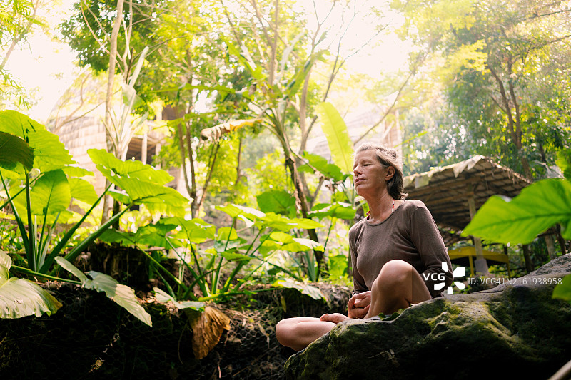 年长的白人女性在浅河边的大石头上冥想图片素材