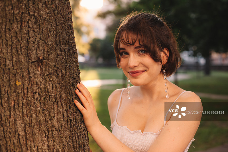 夏天，年轻女子站在城市公园的树旁图片素材