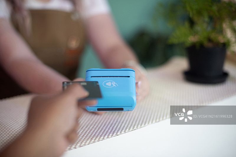 顾客使用银行卡刷卡机支付，在植物苗圃通过金融科技完成交易。在零售店，服务员在金融科技机上点击，顾客用电子设备和POS机支付图片素材