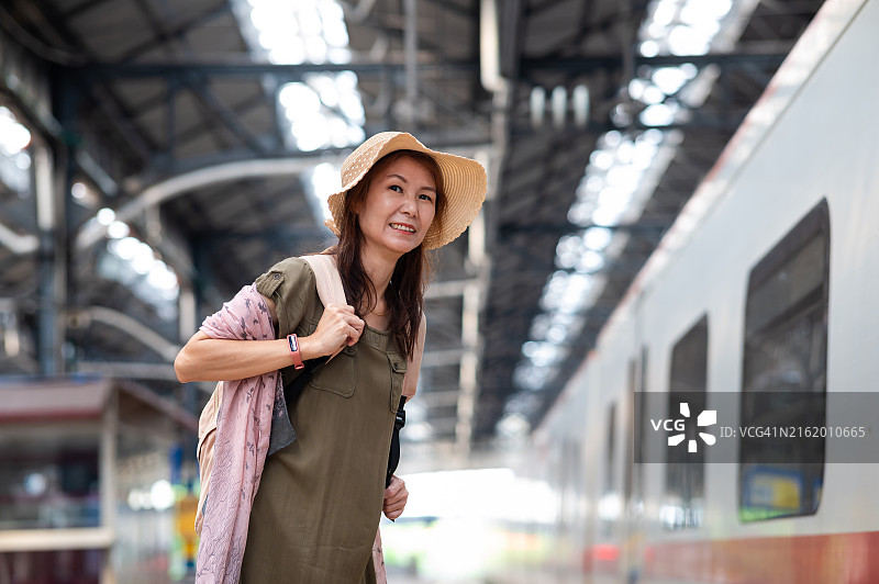 戴着帽子和背包在车站站台等火车的亚洲女性图片素材