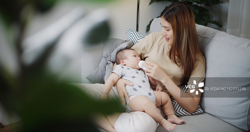 母亲在客厅沙发上用奶瓶喂宝宝图片素材
