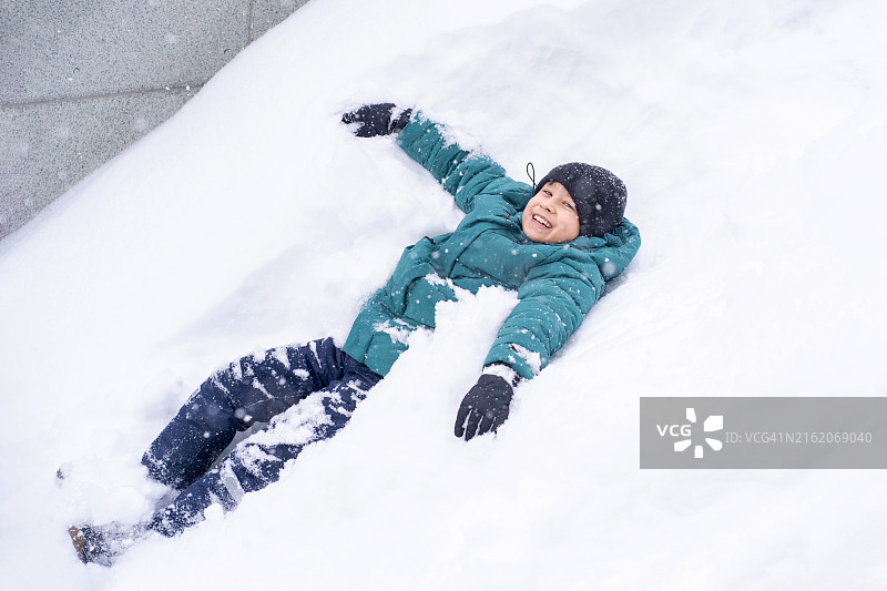 韩国男孩在蓬松的白雪上露出调皮的笑容，享受冬季和雪带来的喜悦图片素材