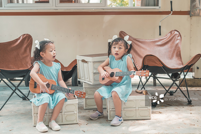 可爱的双胞胎姐妹在户外弹奏尤克里里图片素材