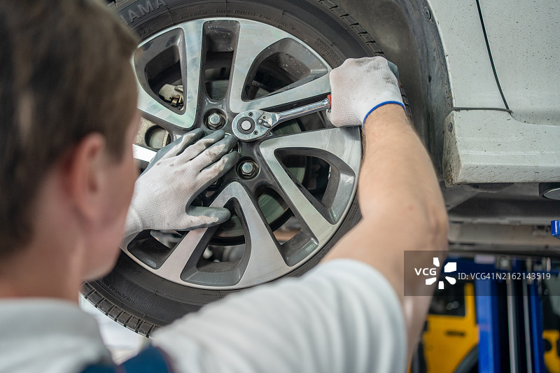 年轻男机械师用钻拧紧汽车轮胎上的螺栓图片素材