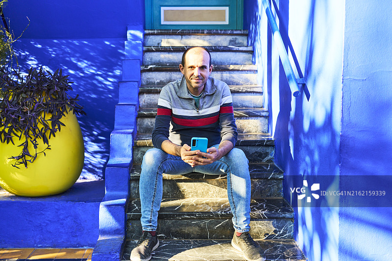 休闲游客男子坐在楼梯上微笑看镜头，手持手机正面照图片素材