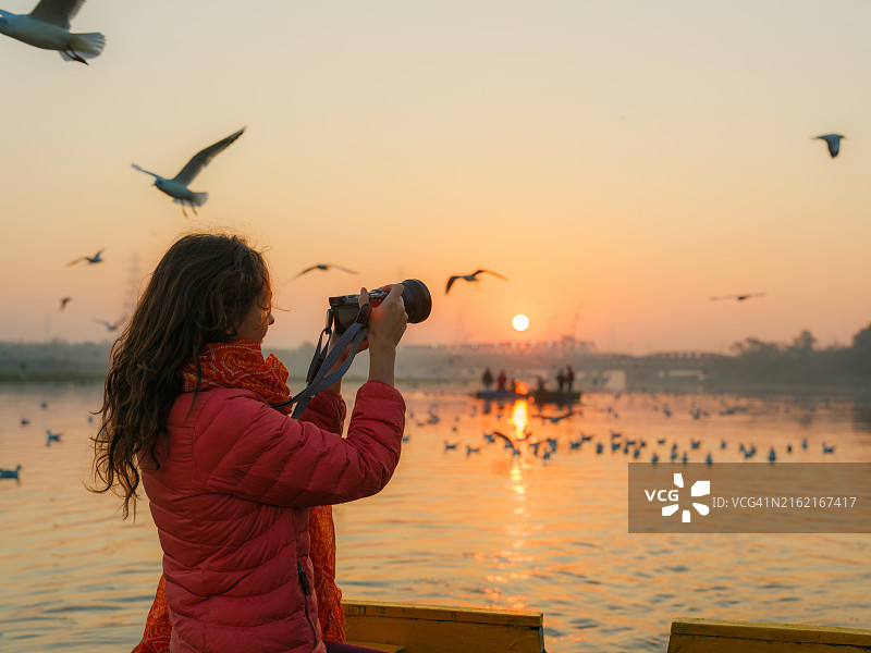 女人在新德里河上从船上用相机拍摄迁徙鸟群图片素材