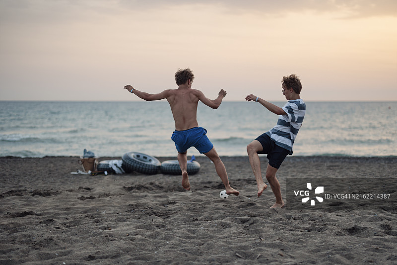 两个青少年男孩在夏日傍晚的沙滩上踢足球图片素材